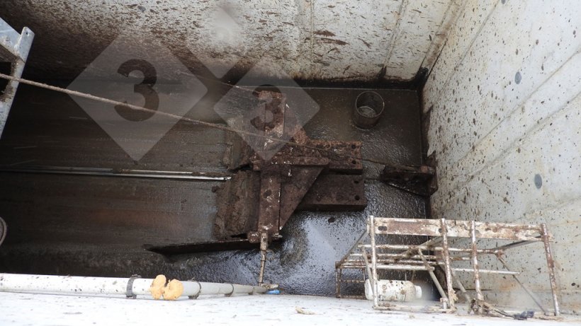 Racleur transversal situ&eacute; au fond du b&acirc;timent qui transporte la pi&egrave;ce solide vers la zone de stockage ext&eacute;rieure.
